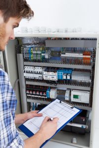 Cropped image of male technician holding clipboard while examining fusebox
