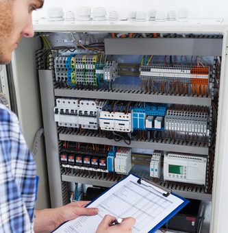 Technician Holding Clipboard While Examining Fusebox
